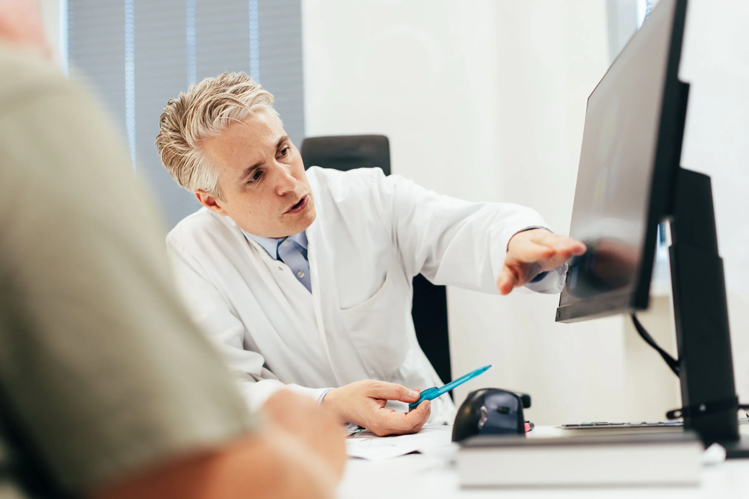 Der Sektionsleiter zeigt einem Patienten am Bildschirm die Aufnahmen der Magnetresonanztomographie.