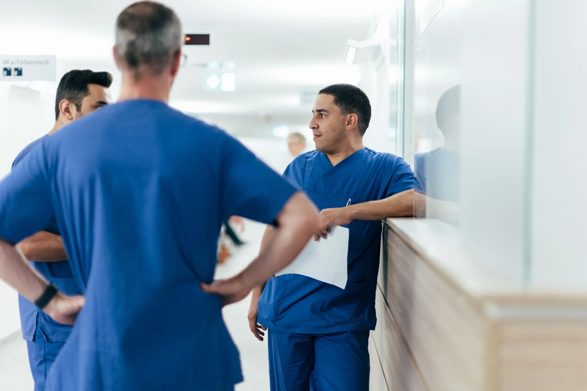 Drei Kolleginnen und Kollegen der Klinik für Urologie besprechen sich in blauer Bereichskleidung auf dem Flur, Unterlagen in der Hand.