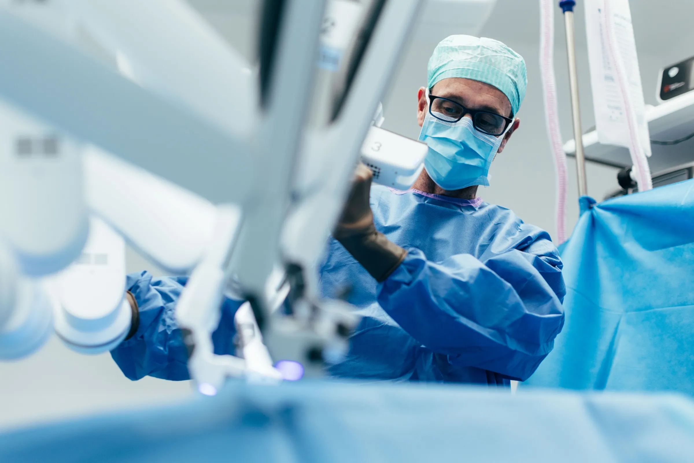 Operateur im sterilen Kittel dockt am Operationstisch einen Instrumentenarm des da Vinci Systems an.