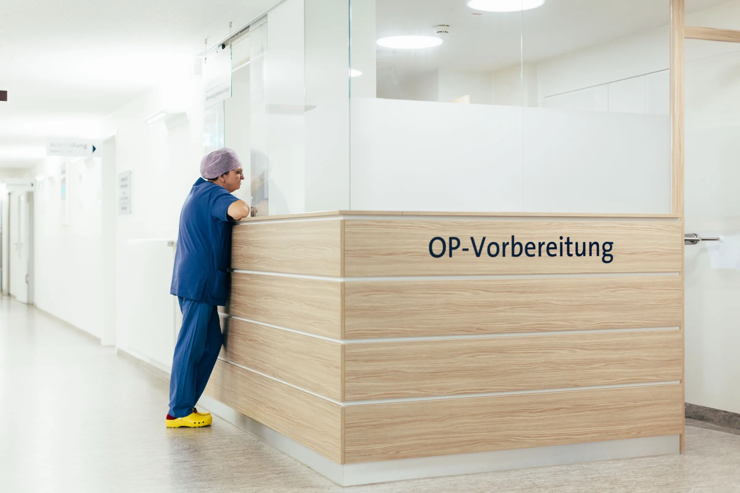 Der Tresen der OP-Vorbereitung auf dem Flur der Klinik; davor steht eine Person in blauer Bereichskleidung.