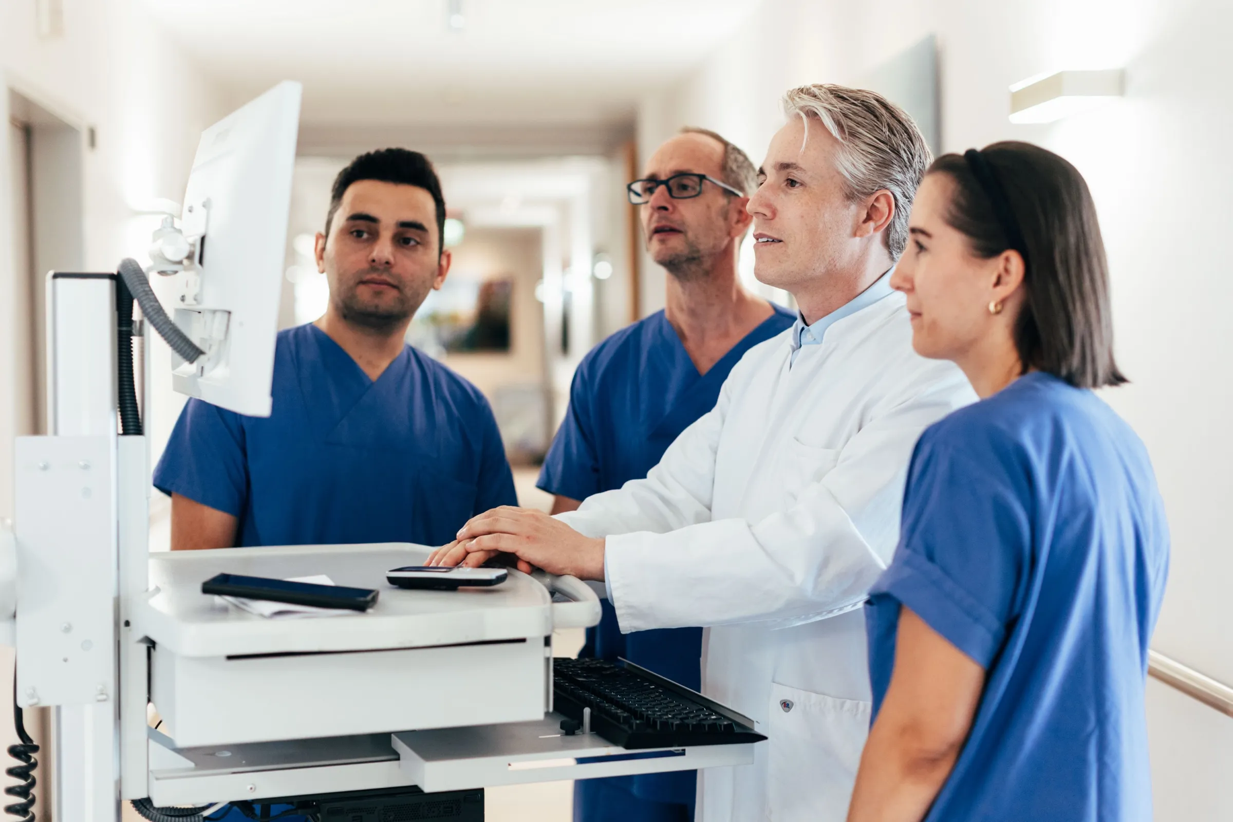 Ärzte und Pflegekräfte der Klinik besprechen auf dem Stationsflur einen Befund am Bildschirm.